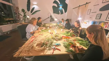 Frauen basteln gemeinsam an einem Tisch mit Pflanzenmaterialien.