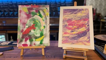 Two paintings stand on easels in a bar.