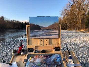 Ein Maler-Kasten mit Landschaftsgemälde am Wasser.