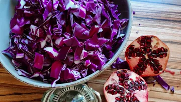 Sliced red cabbage slices in a bowl, with pomegranate halves next to them.