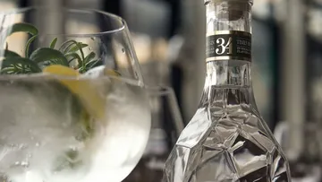 Ein Glas mit Getränk und Gin-Flasche auf Tisch.