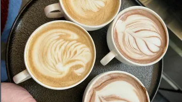 Four cups of coffee with artistic milk froth on a tray.