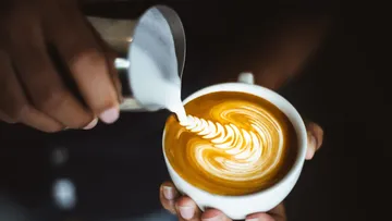Milch wird in eine Tasse mit kunstvollem Kaffee gegossen.