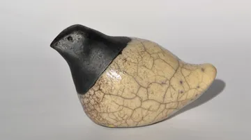 Keramischer Vogel, sitzt still auf einem weißen Hintergrund.