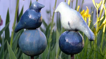 Two ceramic birds sit on round rods.