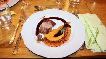 A plate of meat, pumpkin and sauce on wood.