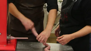 Sausage is prepared while people are helping in a kitchen.