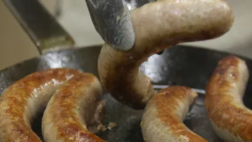 Bratwurst is twisted in a pan using tongs.