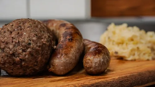 Minced meatballs and sausages lie on a wooden board.