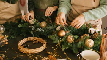 Hände dekorieren einen Adventskranz mit Weihnachtsornamenten.