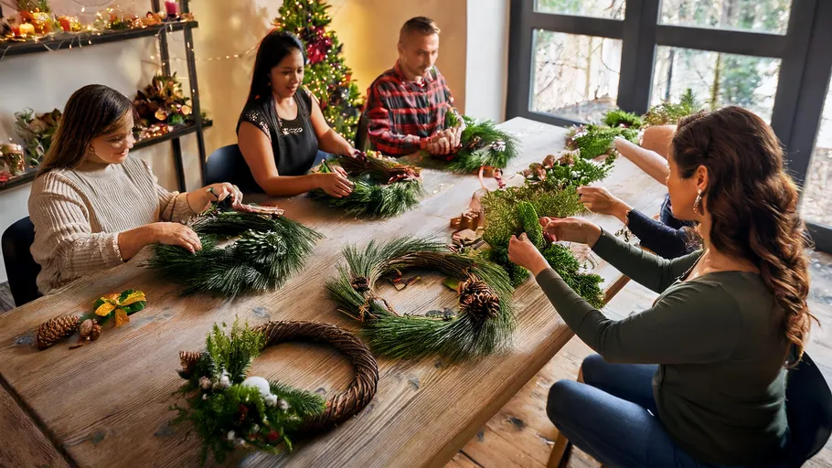 People make Christmas wreaths at the table in a warm environment.