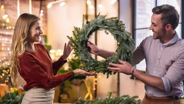 A couple holds a wreath together in a festive room.