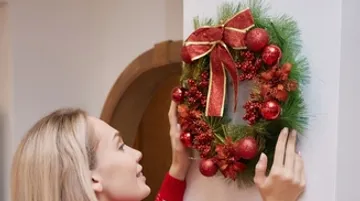 A woman is attaching a Christmas wreath to the wall.