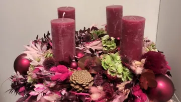 Four red candles stand on a flower arrangement.