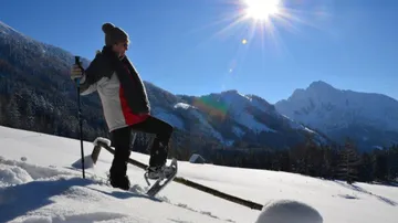 Person geht mit Schneeschuhen durch verschneite Berge bei Sonnenlicht.