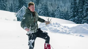 Young man collects branches in a snowy forest.