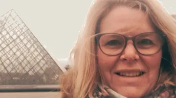Frau lächelt vor Glas-Pyramide im Museum.