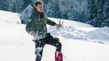A man walks in the snow and carries branches in his hand.