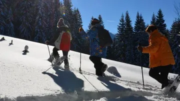 Three people are hiking in snow under a blue sky.