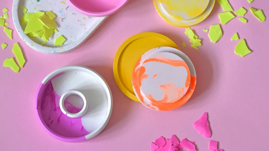 Bunte Farbpaletten liegen verstreut auf einer rosa Fläche.