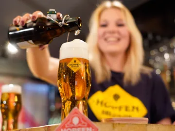 Bierglas wird eingeschenkt, Dame lächelt im Hintergrund.