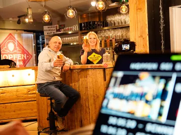 Zwei Personen stoßen an einer Bar mit Biergläsern an.