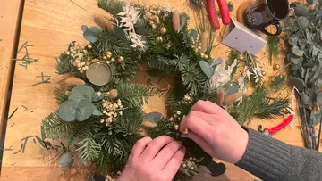 Eine Person dekoriert einen Kranz mit verschiedenen Materialien.
