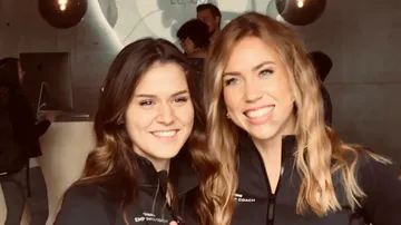 Two women smile warmly in front of a modern reception.