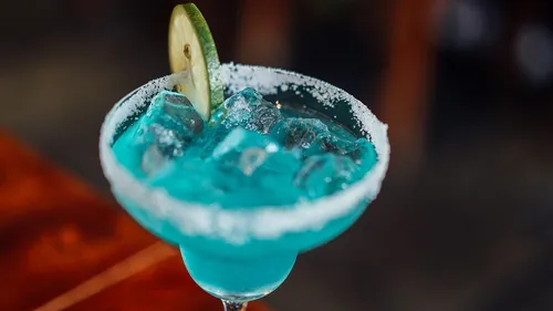 Sparkling blue cocktail with pieces of ice and a slice of lime.