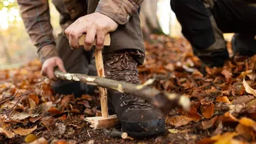 Man carving wooden stick in autumn forest.