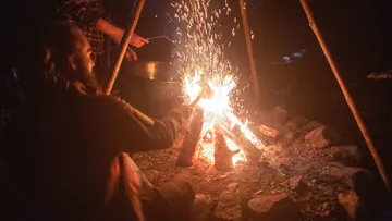 Campfire sparks while someone adds wood.