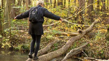 Frau balanciert auf einem Baumstamm in einem Wald.