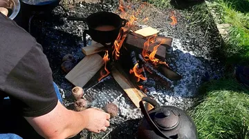 A man cooks over a bonfire with wood.