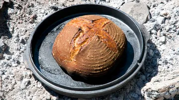 A loaf of bread lies in a cast iron pan.