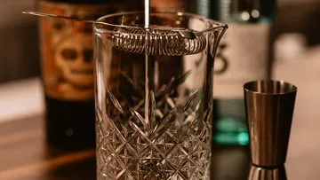 A cocktail shaker from which liquid flows into a glass.