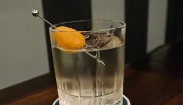 Glas mit klarem Getränk und einer Olive darin.