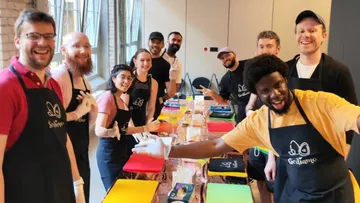 Group laughs and poses in front of colorful painting supplies.