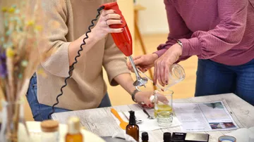 Zwei Personen mixen Zutaten mit einem Stabmixer am Tisch.