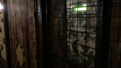 Gittertür mit camouflierter Oberfläche, umgeben von Holz.