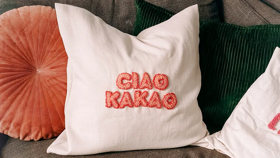 A pillow with red letters “CIAO COCOA” is lying on a couch.