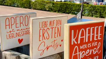 Holzschilder mit kreativen Sprüchen stehen auf einem Tisch.
