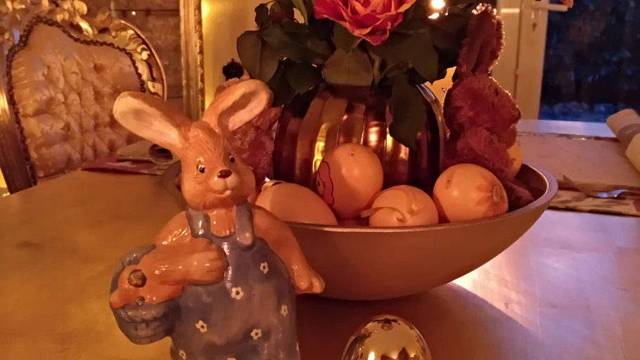 Häschenfigur mit Korb, umgeben von Ostereiern und Blumen.