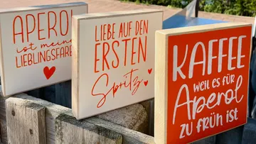 Holzschilder mit bunten Sprüchen auf einer Holzbank.