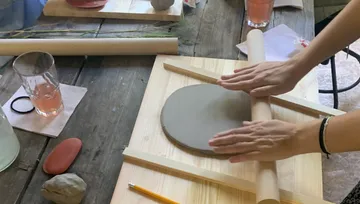 Hands roll clay onto wooden surface in a creative environment.
