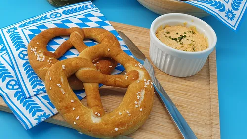 Brezen und Obatzda auf einem Holzbrett und einem blauen Untergrund