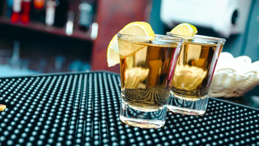 Two glasses of drink stand on a black bar surface.