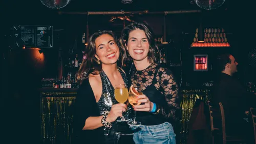 Two women are smiling with drinks in a bar.
