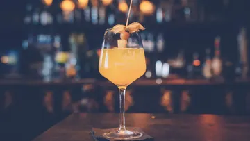 A cocktail in a glass is on the bar.