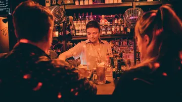 Barkeeperin bereitet Cocktails an einer belebten Bar.