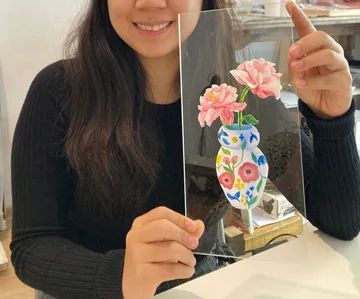Eine Person hält eine bemalte Vase mit Blumen.